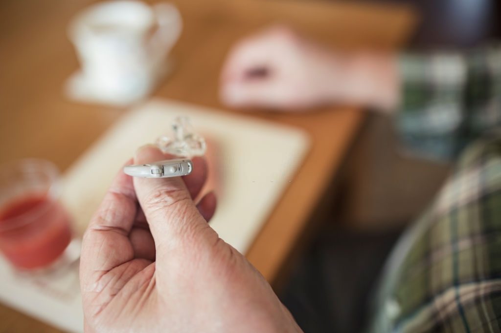Close-up shot of a senior man holding his hearing aid in his hand.