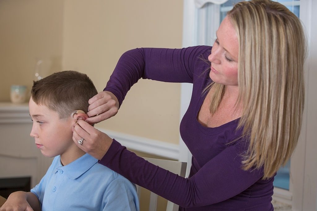 mum helping her kid wearing hearing aid