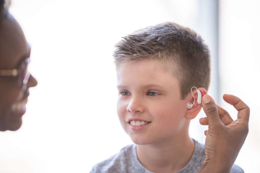 A black female doctor helps a young boy to put in a hearing aid.