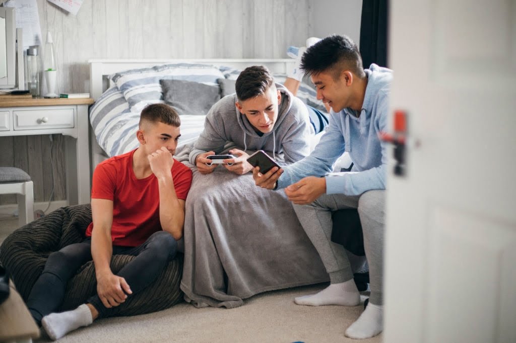 Three teenage boys relaxing and having fun while playing on a games console in a bedroom